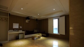A spacious living room with a wooden floor, a sofa, a coffee table, and a large window with blinds. - RIVER HOTEL NAMWON (Namwon)