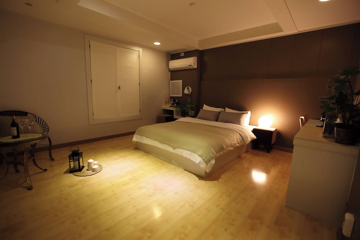 A bedroom with a bed, bedside table, lamp, and a small table with a chair and wine bottle.