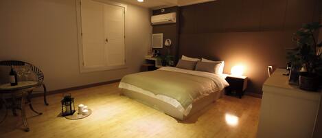 Un dormitorio con cama, mesita de noche, lámpara y una pequeña mesa con una silla y una botella de vino.