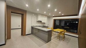 A modern kitchen with a central island, a dining area with yellow chairs, and a large window offering a view of the city at night. - RIVER HOTEL NAMWON (Namwon)