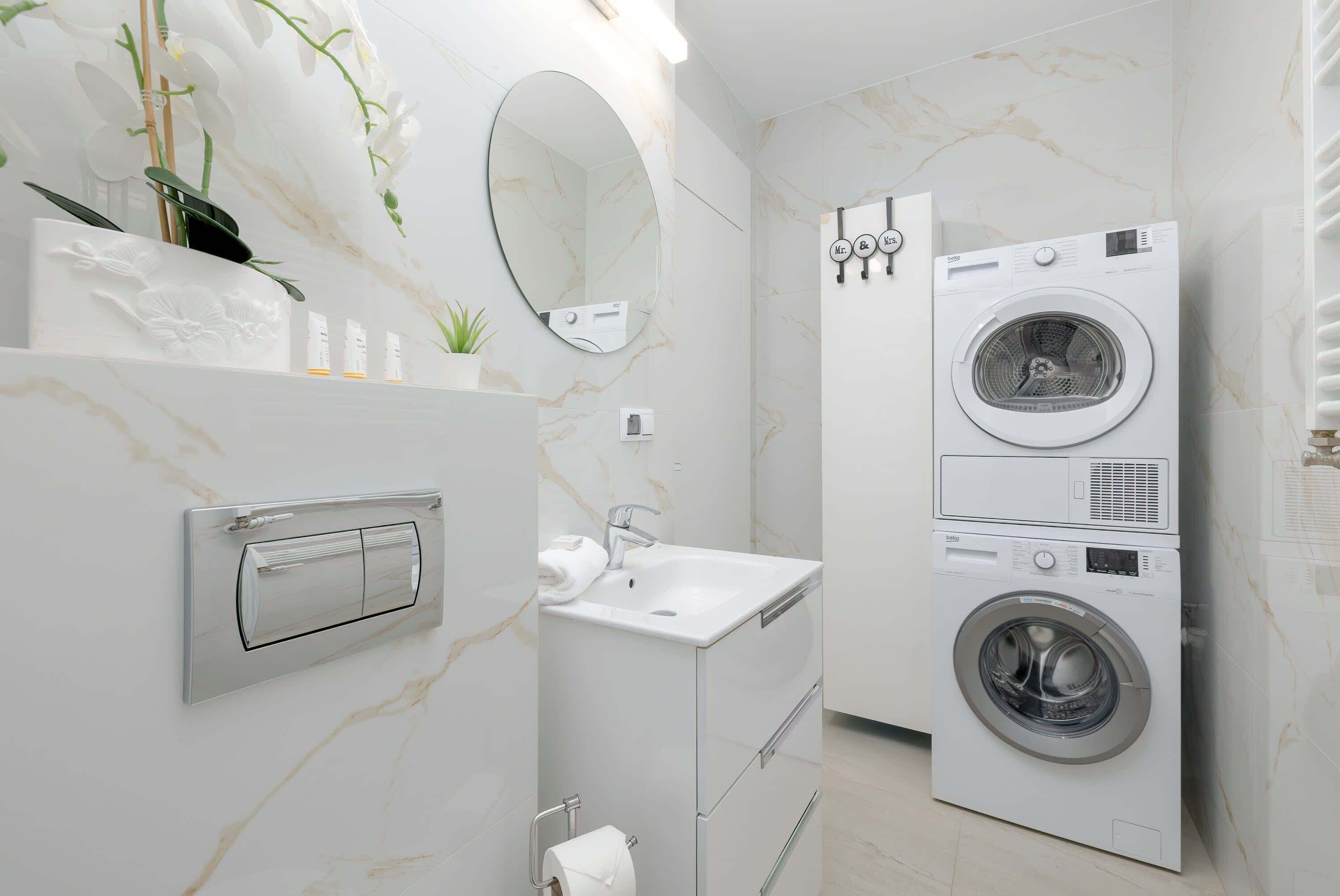 A compact, modern bathroom with a built-in washer and dryer, a mirror, and a small sink.