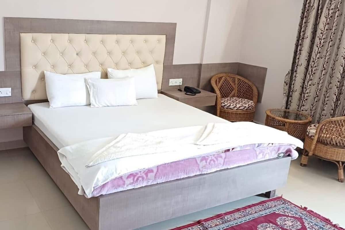 A hotel room with a large bed, a nightstand, a chair, and a patterned curtain.