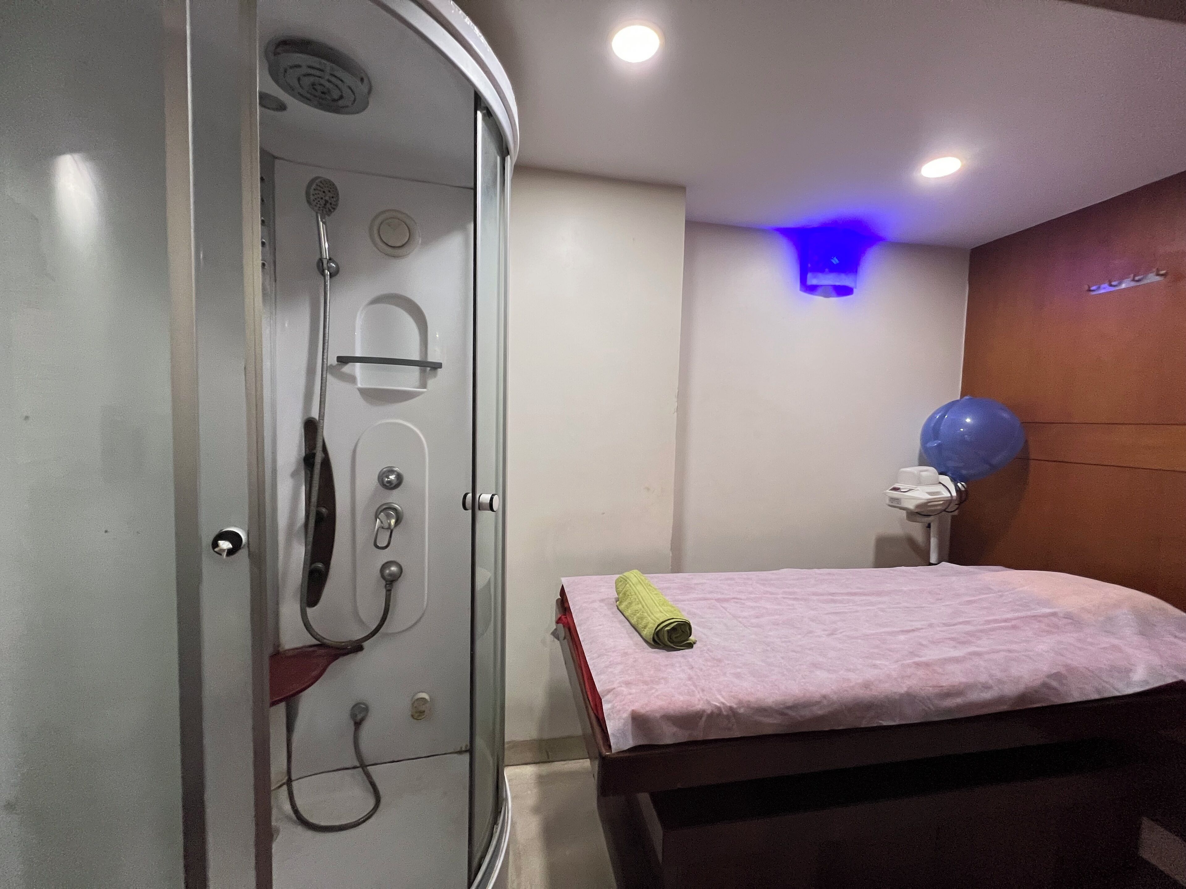 A bathroom with a glass-enclosed shower, a bed with a pink towel, and a blue balloon on a stand.