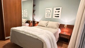 A bedroom with a large bed, a wooden wardrobe, a nightstand with a lamp, and abstract wall art. - J Come Style Surprising 1 Bed in Vila Olimpia (São Paulo)