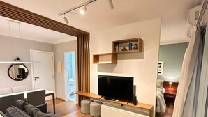 A modern living room with a flat-screen TV, a sofa, and a wooden floor. - J Come Style Surprising 1 Bed in Vila Olimpia (São Paulo)