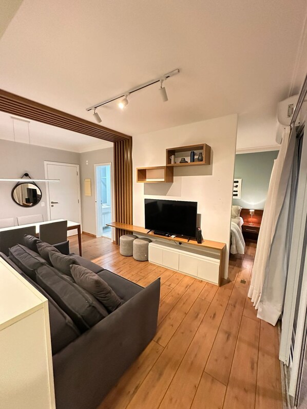 A modern living room with a flat-screen TV, a sofa, and a wooden floor. - J Come Style Surprising 1 Bed in Vila Olimpia (São Paulo)