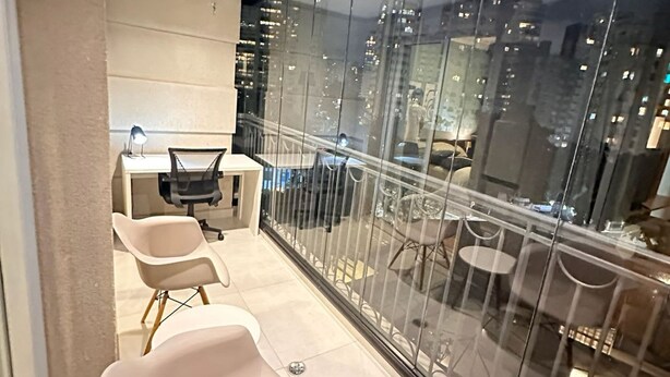A modern balcony with a city view, featuring a seating area with chairs and a small table, and a glass partition. - J Come Style Surprising 1 Bed in Vila Olimpia (São Paulo)