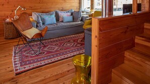 A log cabin interior with a wooden ceiling, a sofa, a chair, a rug, and a fireplace.