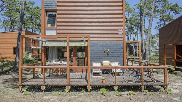 A modern wooden cabin with a deck, outdoor seating, and a bicycle.