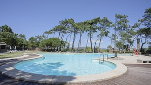 A swimming pool with a wooden deck, surrounded by trees and a clear sky.