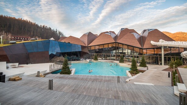 A modern hotel with a pool, wooden deck, and a mountainous backdrop. - Rustic and Radiant Retreat Apartments With Terrace (Podcetrtek)
