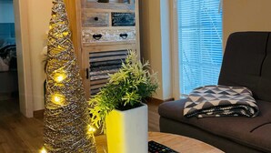 A living room with a decorative Christmas tree, a potted plant, a sofa, and a wooden cabinet with shelves. - Rustic and Radiant Retreat Apartments With Terrace (Podcetrtek)