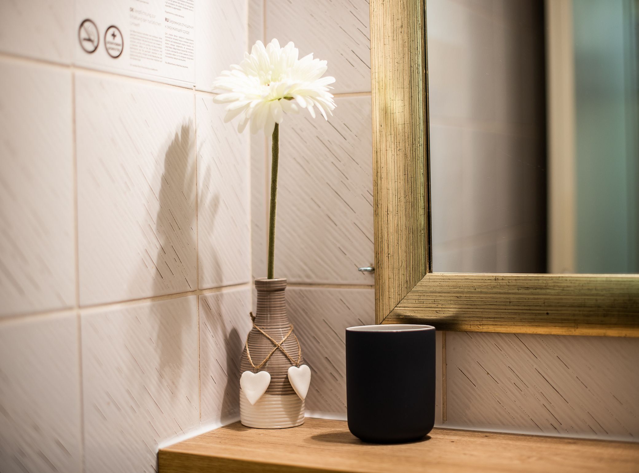 A bathroom with a white flower in a striped vase, a black container, and a mirror.