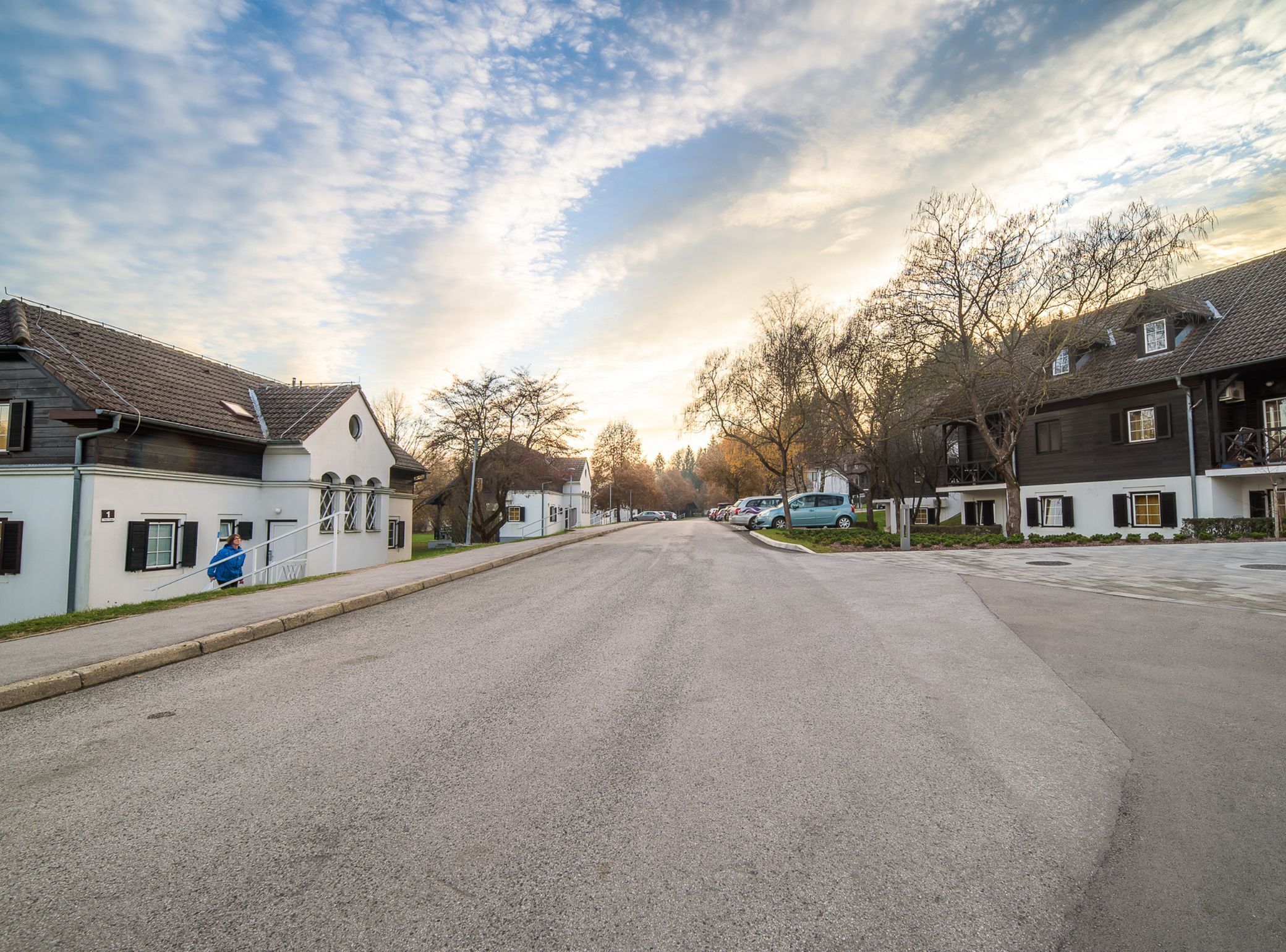A residential street with houses on both sides, a clear sky, and parked cars.