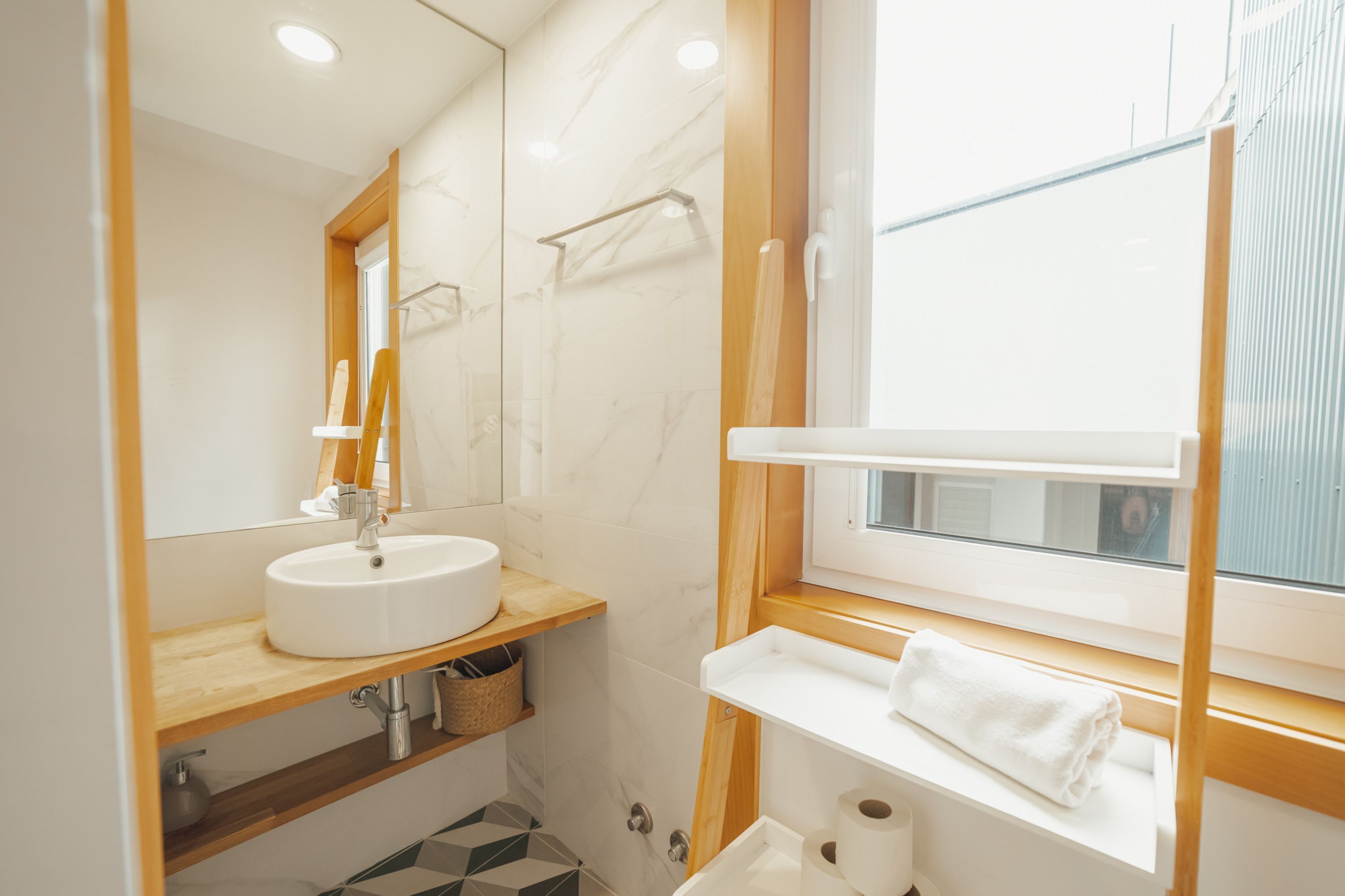Un baño moderno con un lavabo blanco, estantes de madera, un espejo y una ventana.