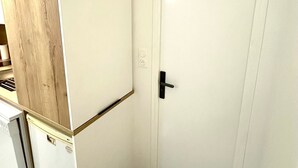 Une cuisine de taille réduite, avec un réfrigérateur blanc, un meuble en bois et une porte blanche dotée d’une poignée noire.