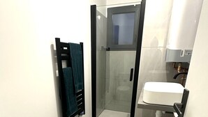 Une salle de bain moderne avec une douche à parois de verre, des toilettes blanches et un lavabo surmonté d’un miroir.