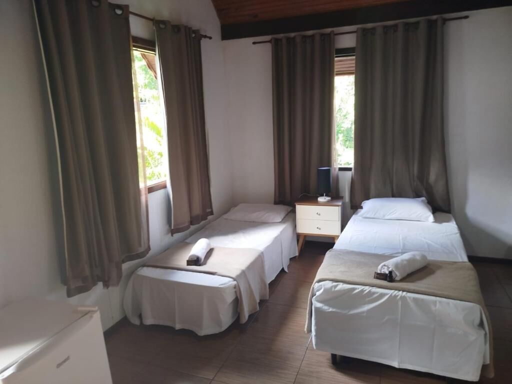 A room with two single beds, a small table, a nightstand, and a window with curtains.