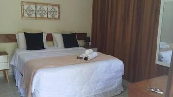 Quarto de hotel com cama grande, duas mesas de cabeceira, cabeceira de madeira, pequena escrivaninha e um espelho.