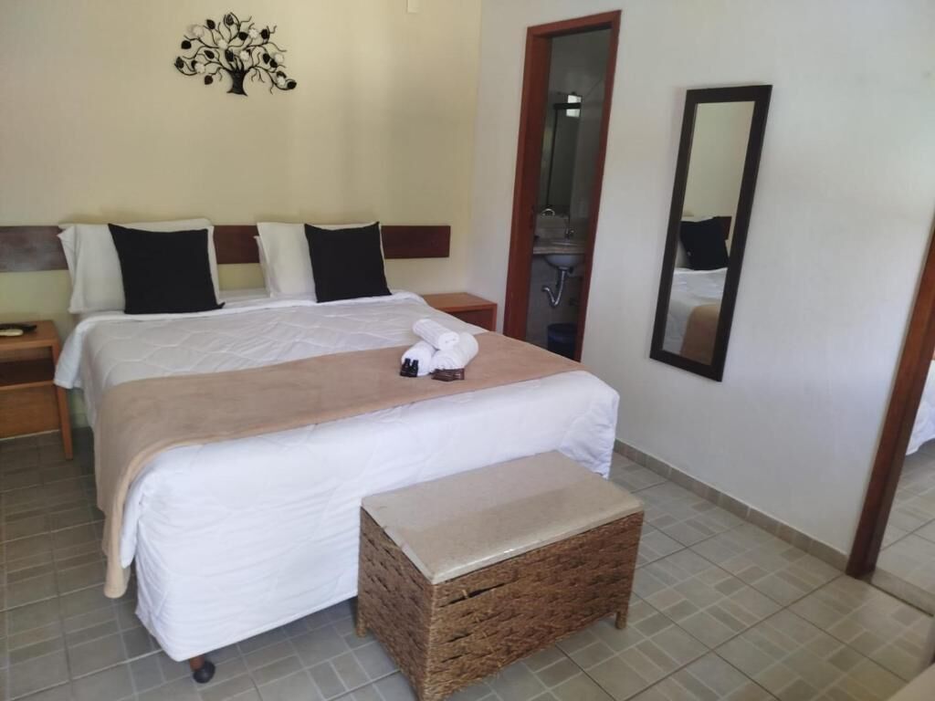 Quarto de hotel com duas camas, um banco de madeira, um espelho e uma decoração de árvore fixada na parede.