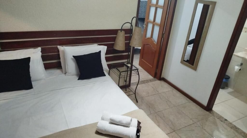 A hotel room with a bed, pillows, a lamp, a mirror, and a bathroom visible through an open door.