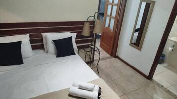 A hotel room with a bed, pillows, a lamp, a mirror, and a bathroom visible through an open door.