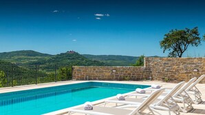 Una piscina con agua cristalina azul, rodeada de muros de piedra y sillones blancos.