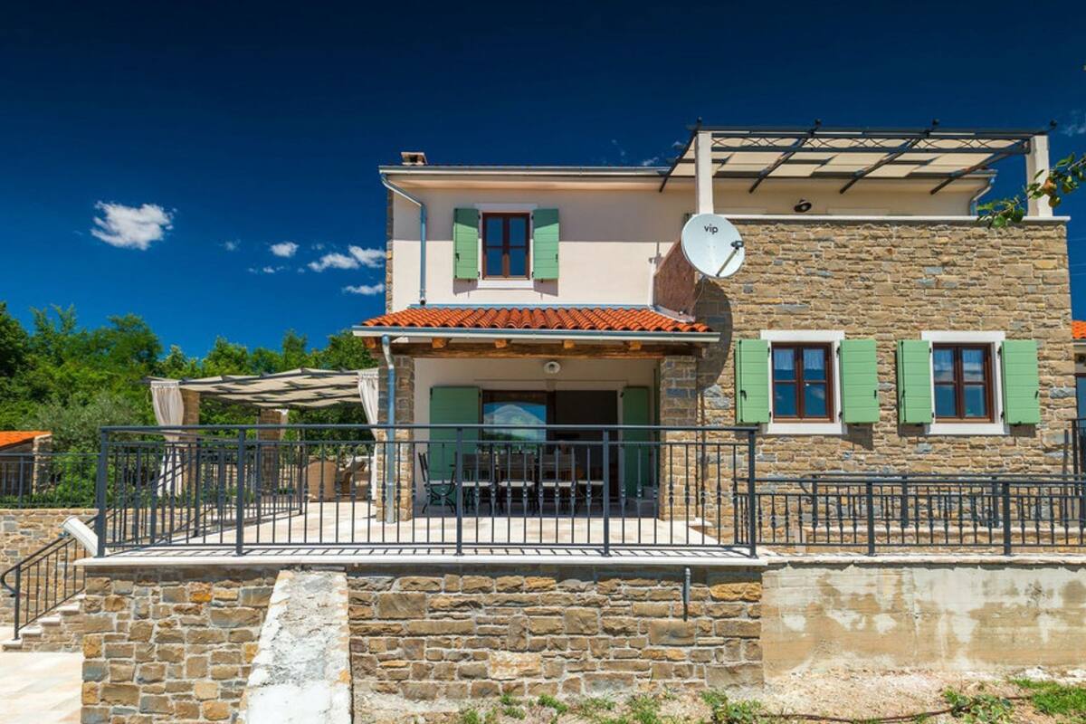 A two-story house with a stone facade, a tiled roof, and a balcony with a metal railing.