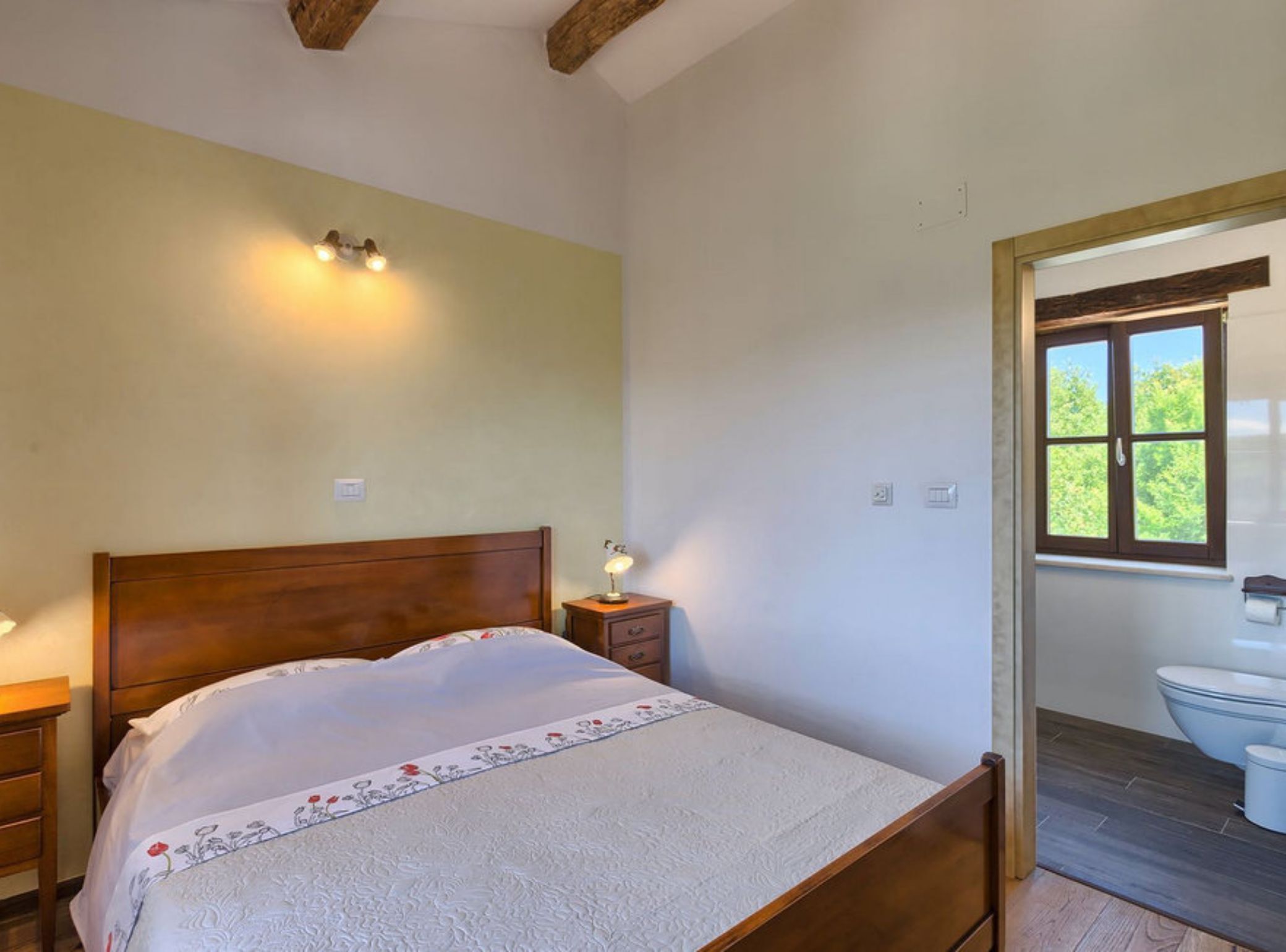 A bedroom with a wooden bed, bedside lamps, a nightstand, and a window with a view of the outdoors.