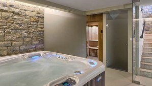 Un baño moderno con pared de piedra, ducha con cerramiento de vidrio y bañera de hidromasaje.