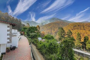 A pathway leading to a building with a stone facade, surrounded by lush greenery and mountains in the background. - Neem Karoli Green valley luxury Villa (Nainital)
