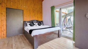 Ein Schlafzimmer mit Holzboden, einem Bett mit schwarz-weißer Bettwäsche, einer Glastür zum Außenbereich und einem kleinen Tisch mit Stuhl.