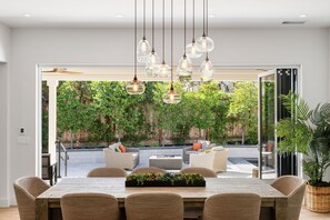 A modern dining area with a large table, wicker chairs, and hanging pendant lights. - In-Town Hideaway on Quiet Lane (St. Helena)