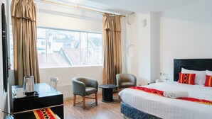 Una camera d'albergo con un letto, due poltrone, un tavolino, una macchina per il caffè e vista sulla città da ampie finestre.