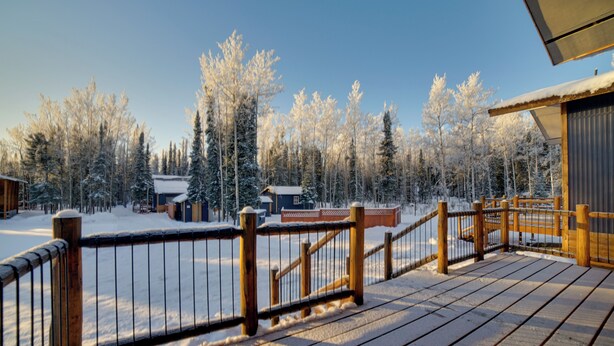 Une terrasse en bois avec une rambarde en métal, donnant sur un paysage enneigé parsemé d’arbres et de bâtiments.