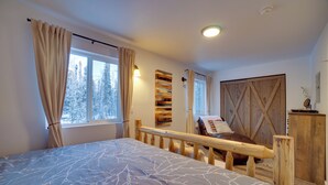Une chambre à coucher avec un grand lit, une tête de lit en bois, un banc en bois, une armoire et une fenêtre avec des rideaux.
