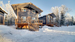 Une cabane en bois avec un escalier menant à une terrasse, entourée d’arbres couverts de neige.