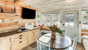 A wooden interior with a kitchen area, dining table, and a television mounted on the wall. - 4 Mi to Main Street: Riverfront Minnesota Cabin (Elk River)