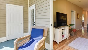 A room with a wicker chair, a television on a white cabinet, and a door leading to another room. - Pond Views & Community Perks: Sunset Beach Condo! (Sunset Beach)