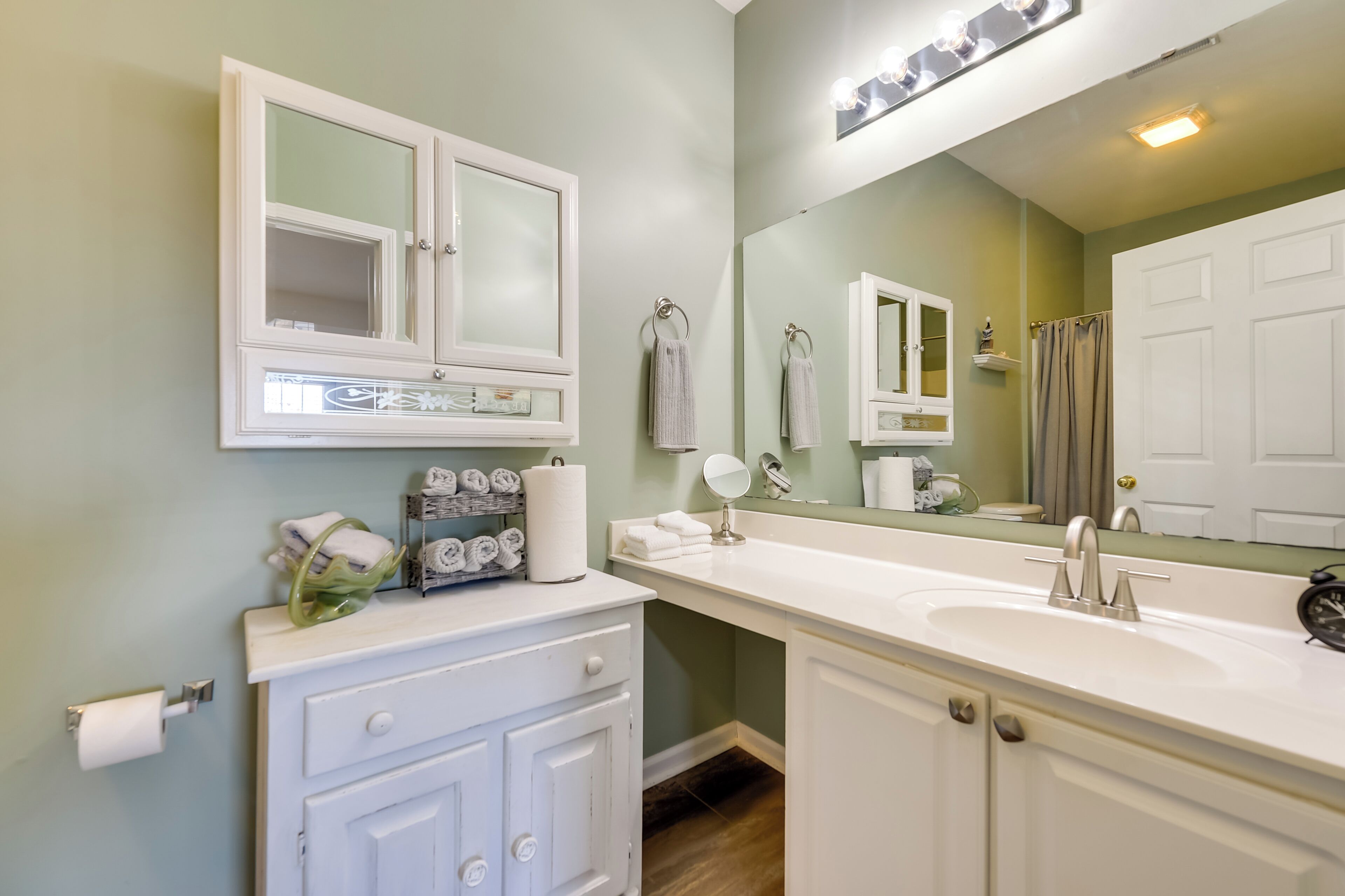 A bathroom with a white vanity, a large mirror, and a white sink.