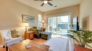 A living room with a ceiling fan, a sofa, a coffee table, a TV, and a large window with a view. - Pond Views & Community Perks: Sunset Beach Condo! (Sunset Beach)