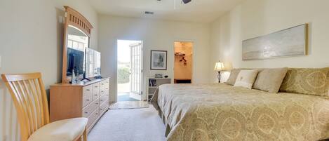 A bedroom with a bed, a chair, a dresser, a ceiling fan, a painting, and a window.