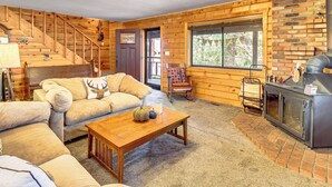 Ein gemütliches Blockhaus-Interieur mit einer Holztreppe, einem Kamin, einem Sofa mit einem Deer-Kissen und einem Schaukelstuhl.
