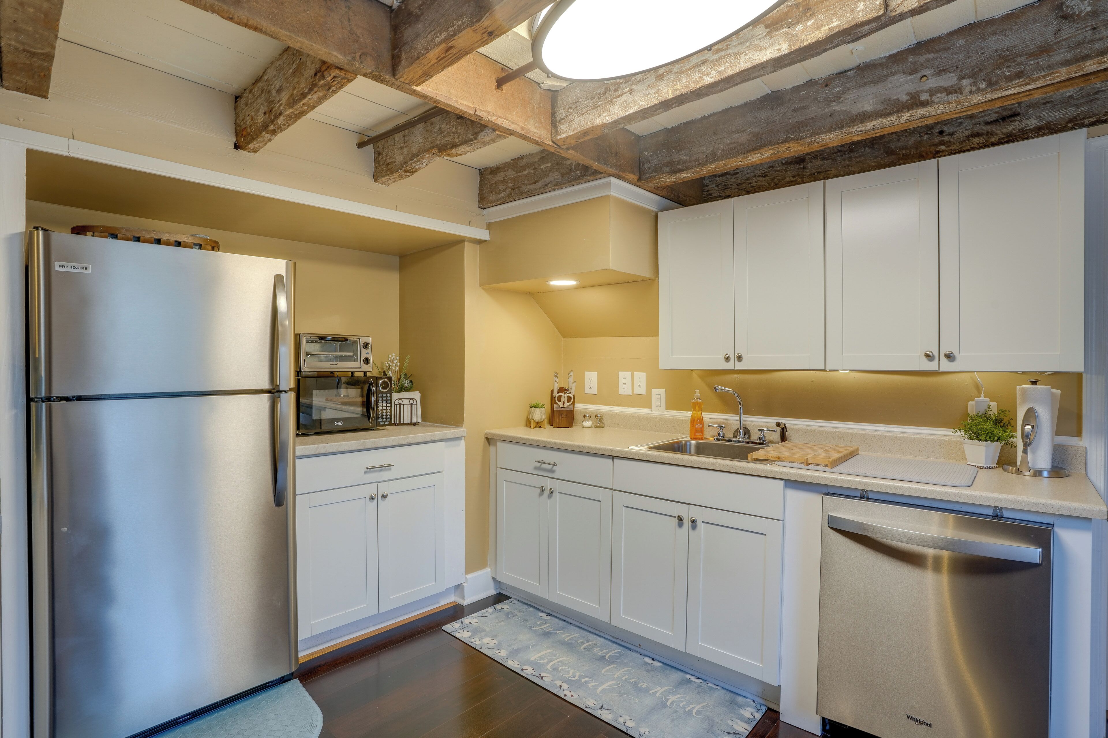A modern kitchen with white cabinets, stainless steel appliances, and a wooden ceiling.