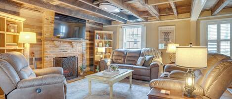 A cozy living room with a fireplace, leather sofas, a flat-screen TV, and wooden beams on the ceiling.