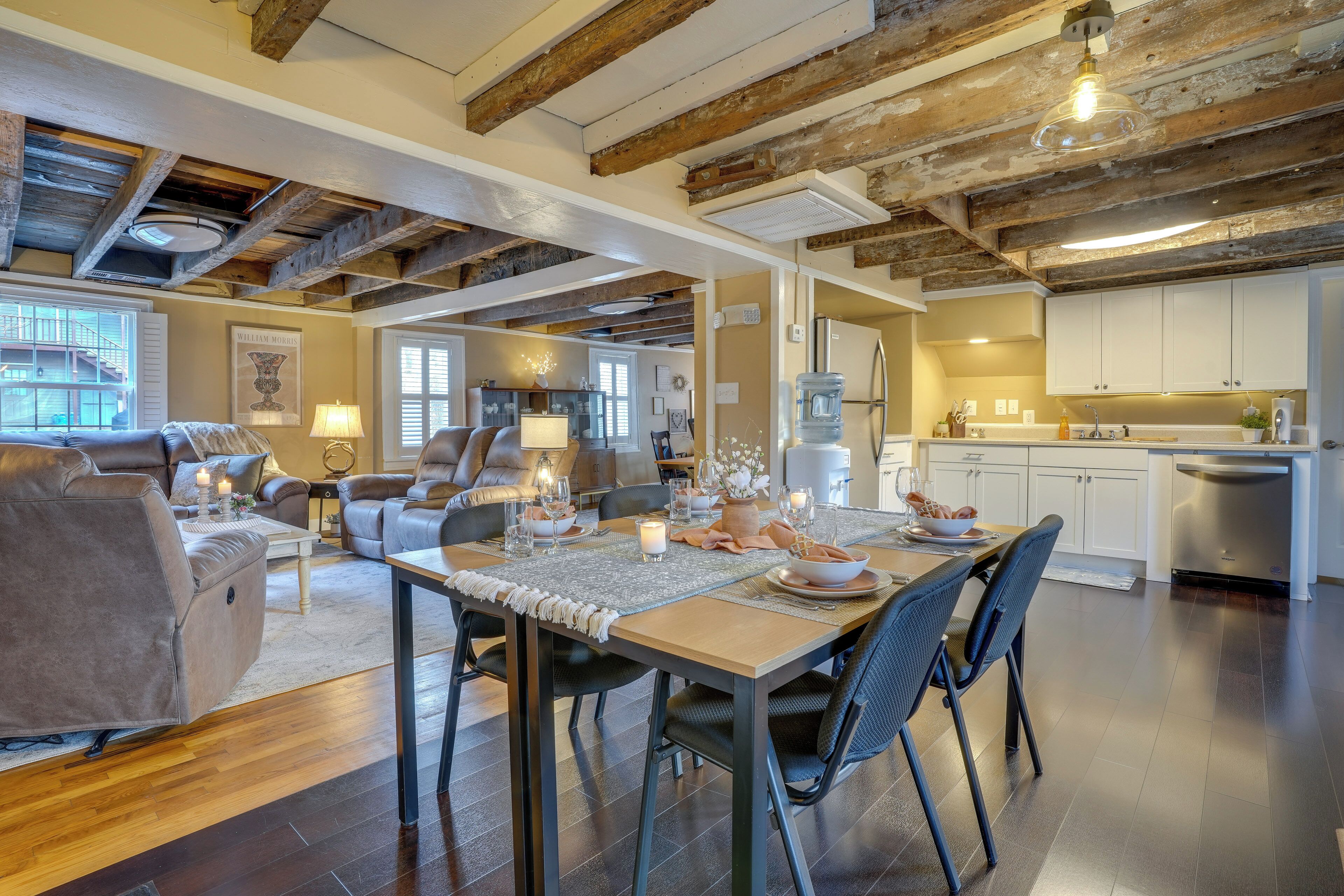 A spacious living room with a dining area, wooden beams on the ceiling, and a modern kitchen in the background.