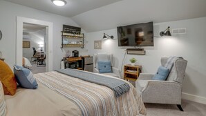 Ein modernes Schlafzimmer mit einem großen Bett, zwei Sesseln, einem Schreibtisch und einem Fernseher.