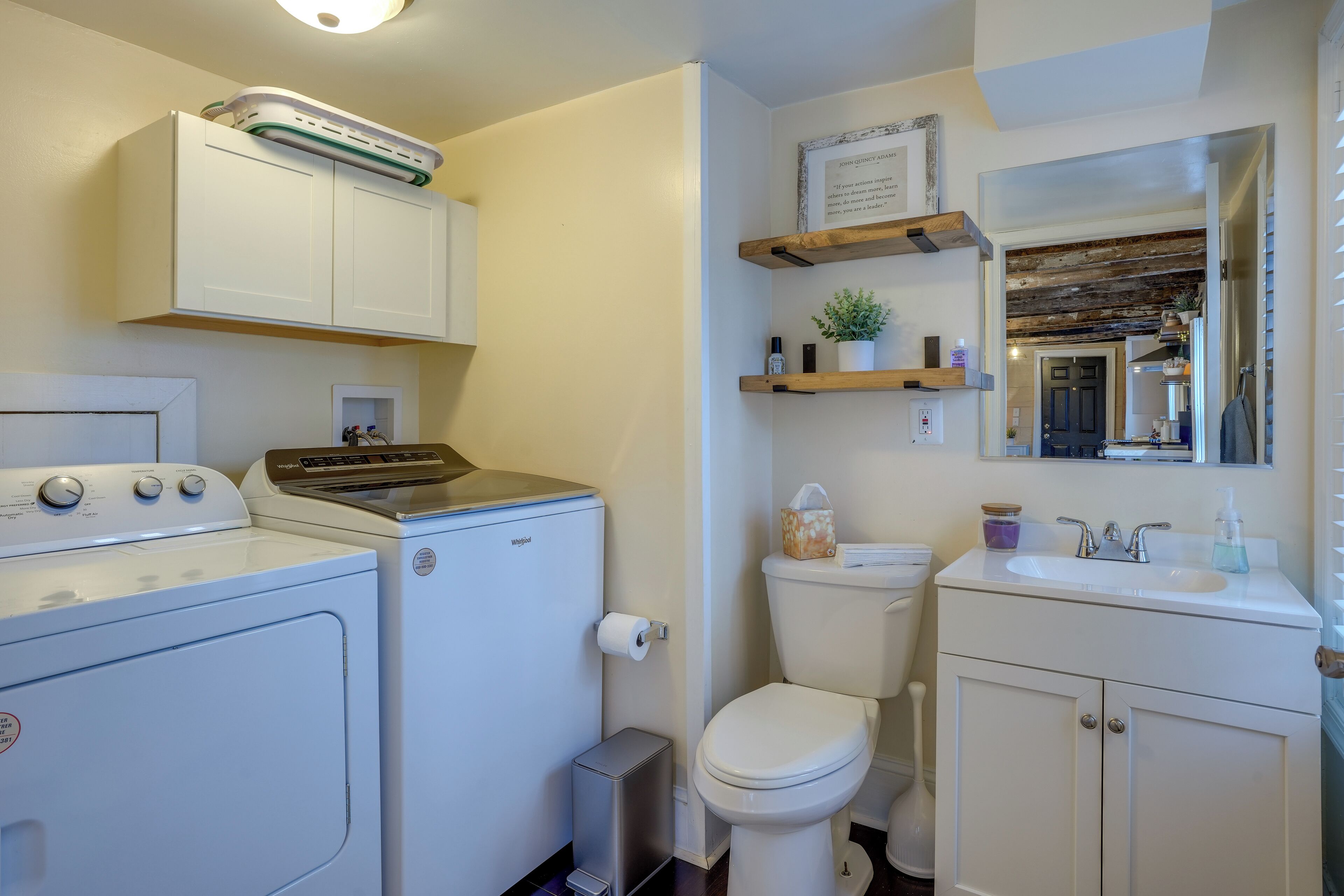A compact bathroom with a washing machine, a toilet, a sink, and a mirror.