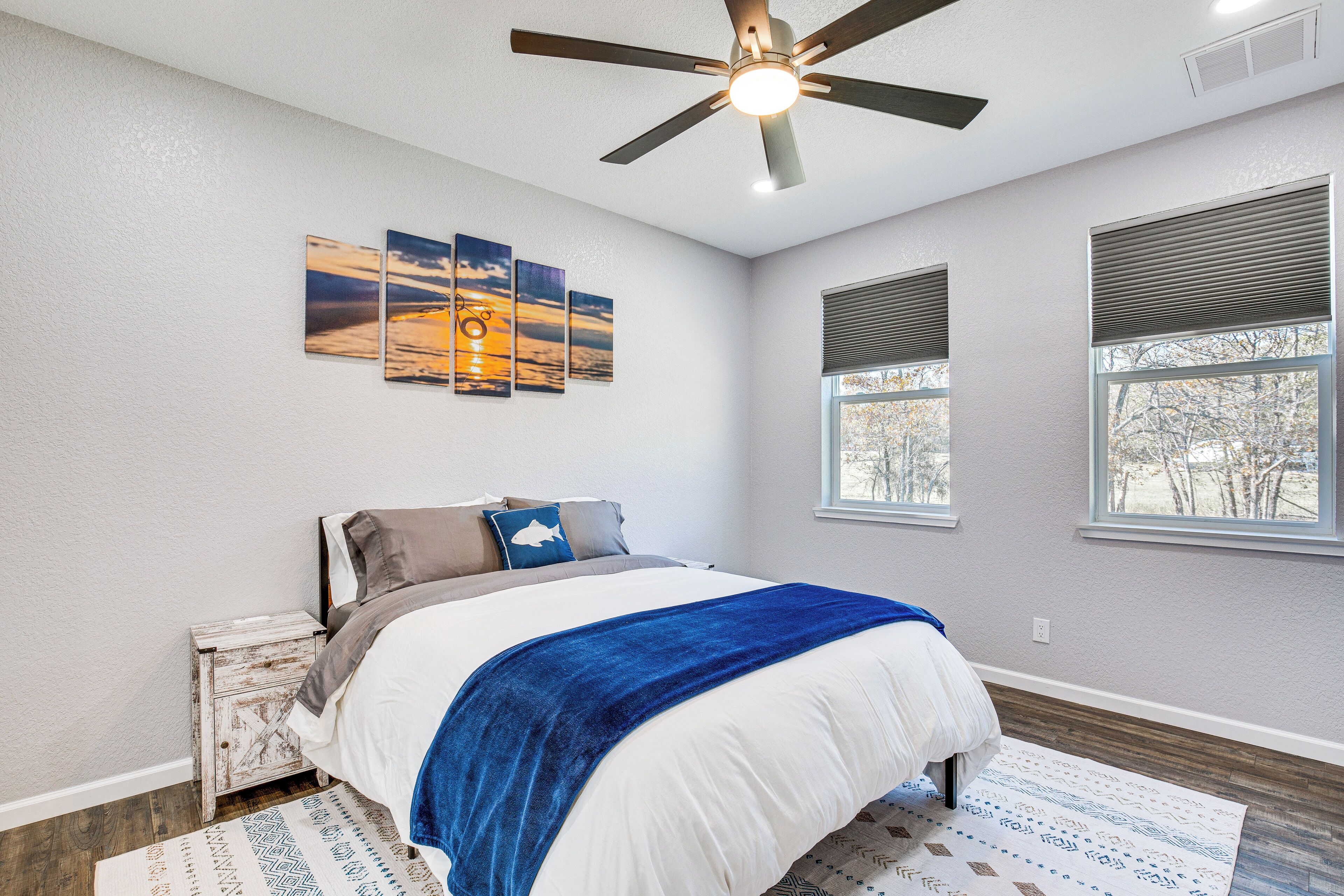 A bedroom with a bed, a ceiling fan, a nightstand, a window, and a wall-mounted artwork.