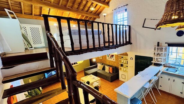 Un intérieur à plusieurs niveaux, avec un escalier en bois, un ensemble de canapés, un coin cuisine et une table à manger.